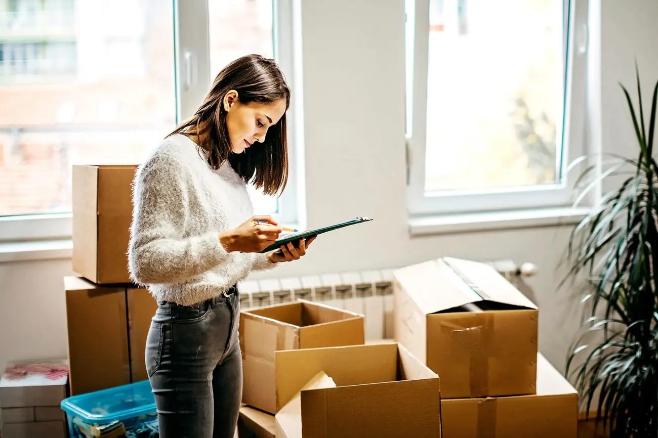 a woman writing on a clipboard in a room with boxes
